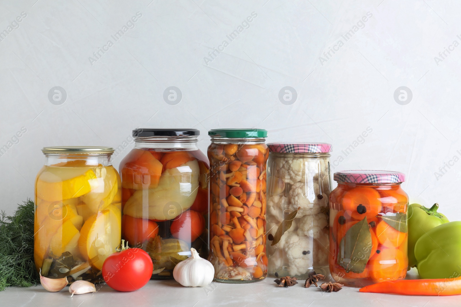 Photo of Fresh vegetables and jars of pickled products on light grey table