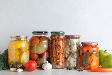 Photo of Fresh vegetables and jars of pickled products on light grey table