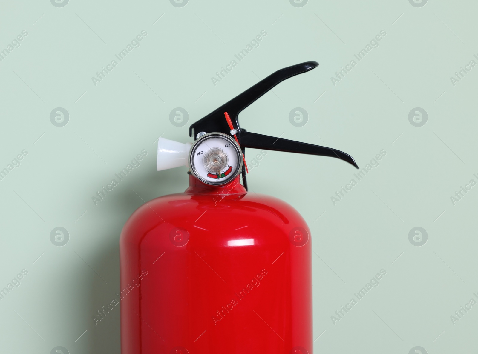 Photo of Red fire extinguisher on light green background, closeup. Space for text
