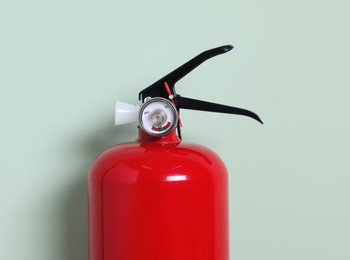 Red fire extinguisher on light green background, closeup. Space for text