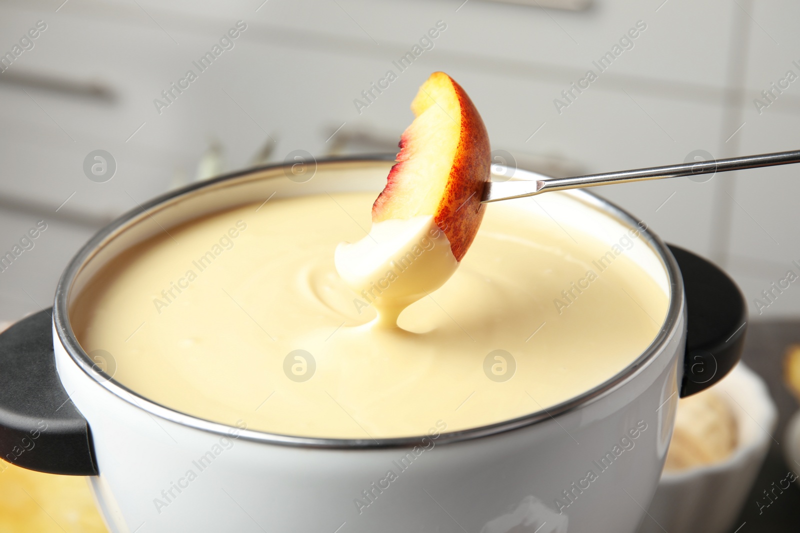 Photo of Dipping fresh peach into pot with chocolate fondue, closeup