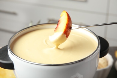 Dipping fresh peach into pot with chocolate fondue, closeup