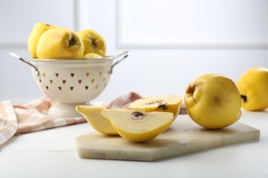 Tasty ripe quinces and metal colander on white wooden table
