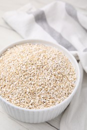 Dry barley groats in bowl on white wooden table, closeup