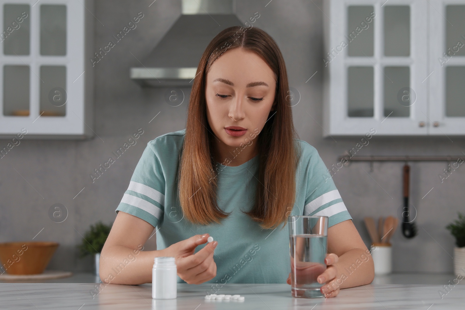 Photo of Depressed woman with glass of water and antidepressant pills at table in kitchen