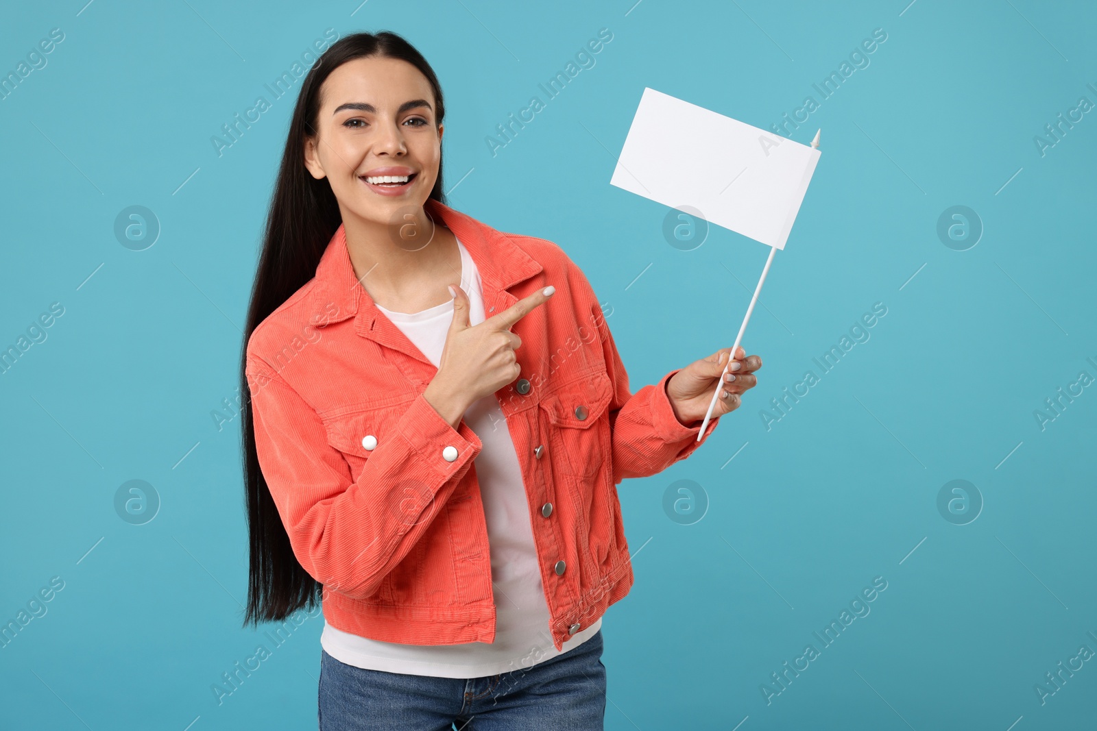 Photo of Happy young woman pointing at blank white flag on light blue background. Mockup for design