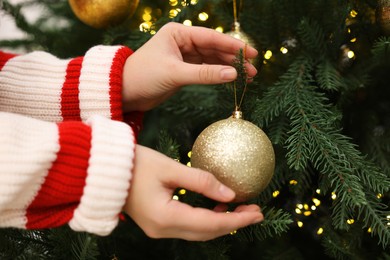 Photo of Woman decorating fir tree with golden Christmas ball, closeup