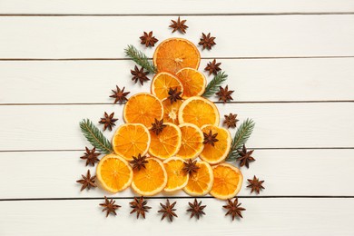 Photo of Flat lay composition with dry orange slices, fir branches and anise stars arranged in shape of Christmas tree on white wooden table