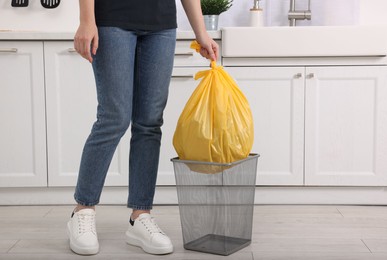 Photo of Woman taking garbage bag out of trash bin in kitchen, closeup