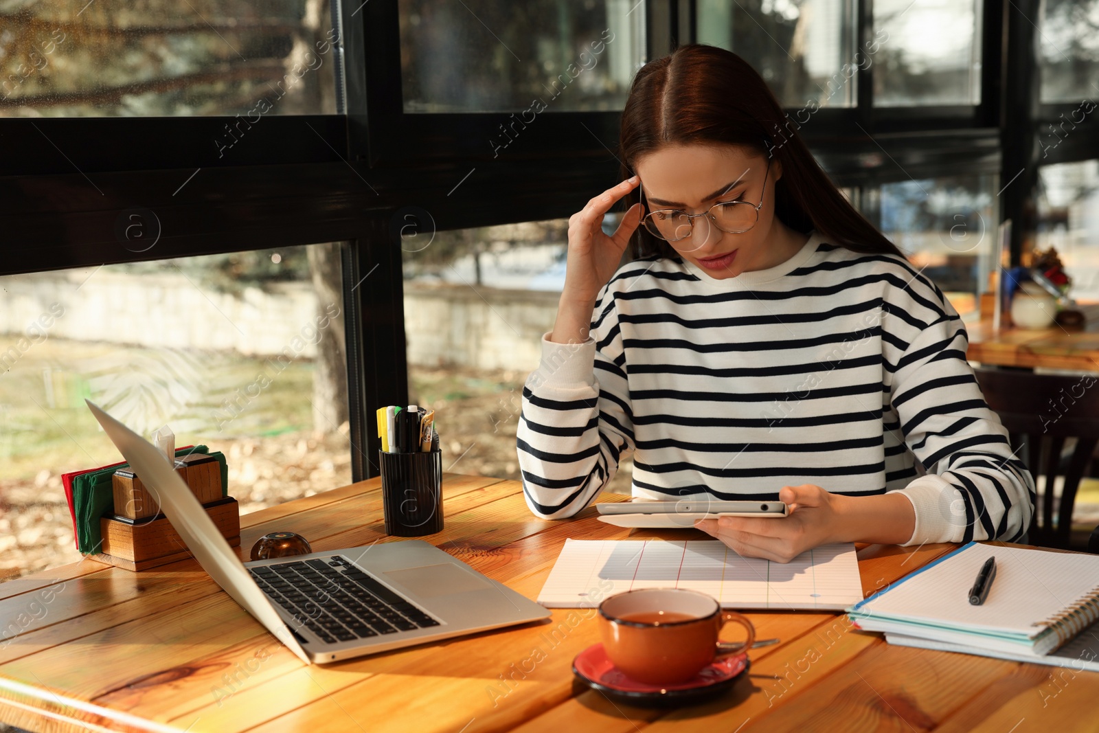 Photo of Young female student with laptop and tablet studying at table in cafe