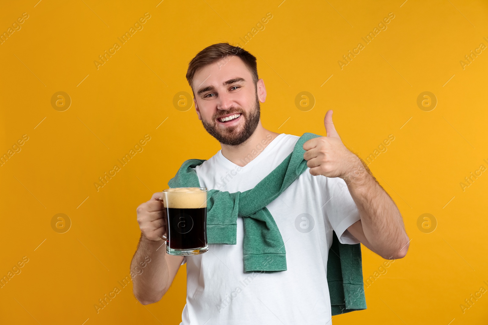 Photo of Handsome man with cold kvass on yellow background. Traditional Russian summer drink