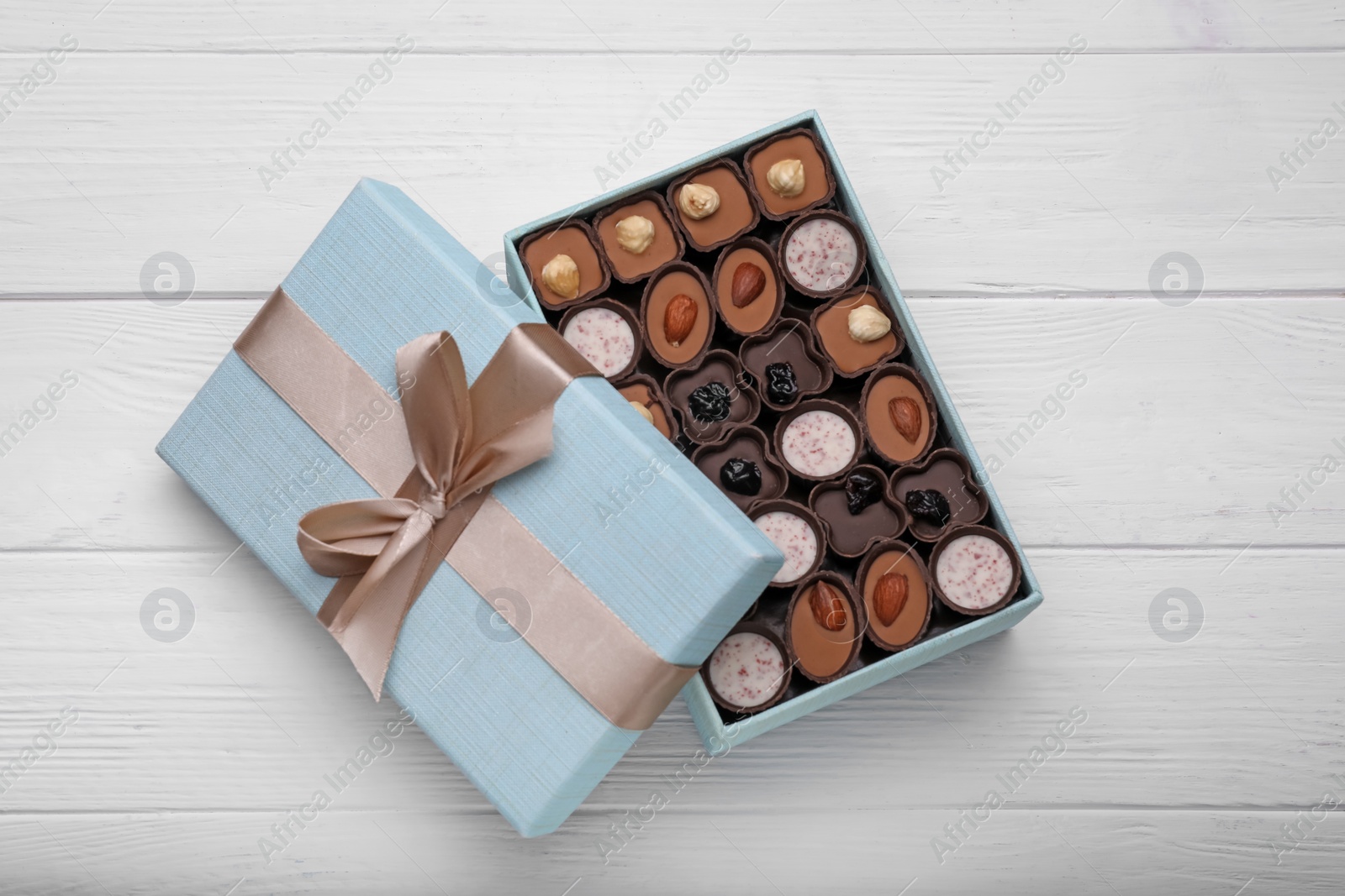 Photo of Open box of delicious chocolate candies on white wooden table, top view