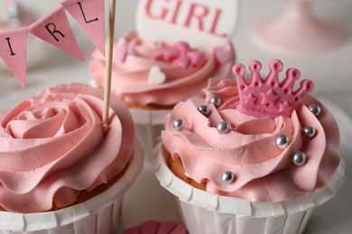 Photo of Delicious cupcakes with pink cream and toppers for baby shower, closeup