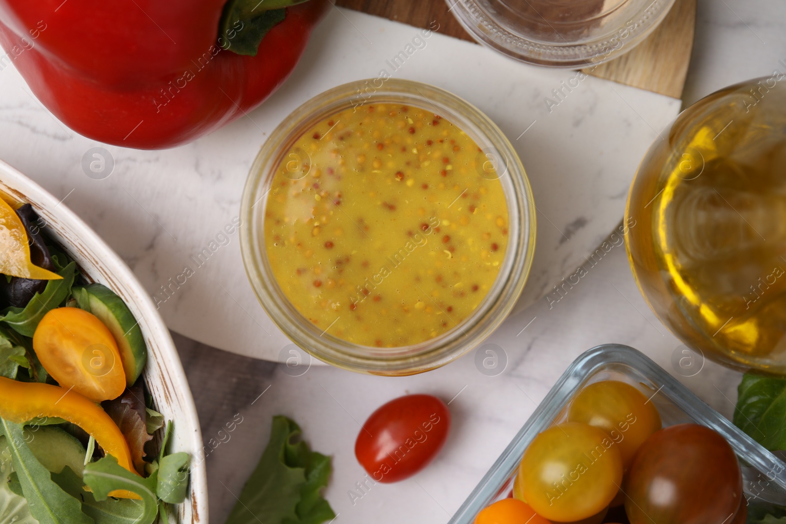 Photo of Tasty vinegar based sauce (Vinaigrette) in jar, salad and products on white marble table, flat lay