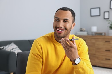 Photo of Happy man sending voice message via smartphone indoors