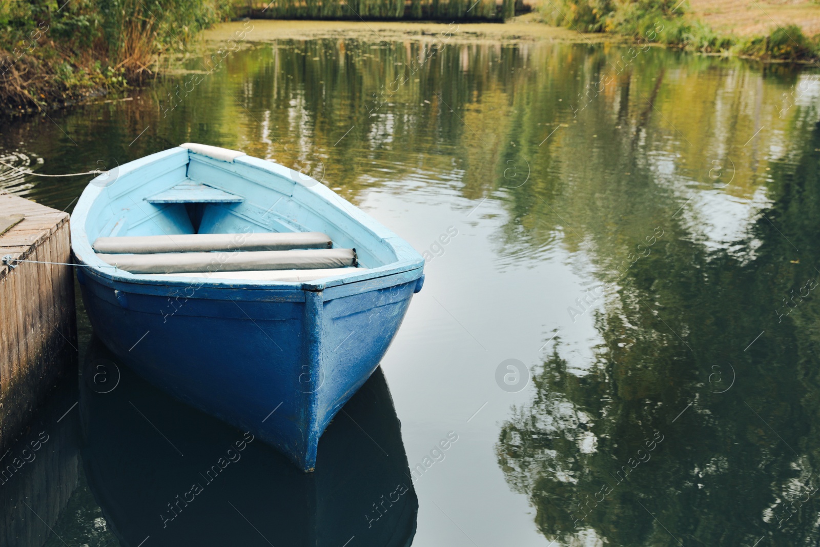 Photo of Light blue wooden boat on lake near pier, space for text