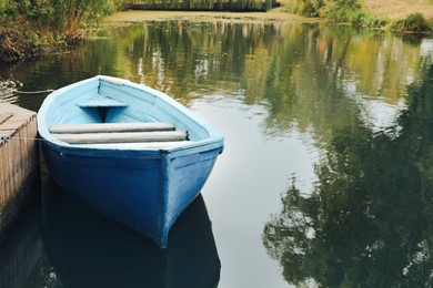 Light blue wooden boat on lake near pier, space for text