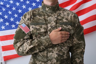 Photo of Soldier holding hand on heart near United states of America flag on white background, closeup