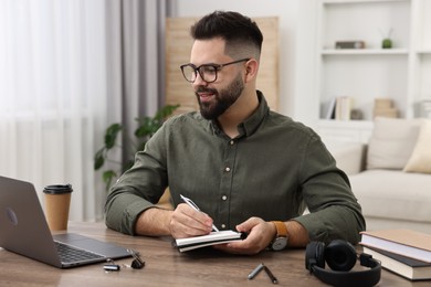 E-learning. Young man taking notes during online lesson at wooden table indoors