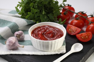 Photo of Organic ketchup in bowl, fresh tomatoes, parsley and garlic on table. Tomato sauce