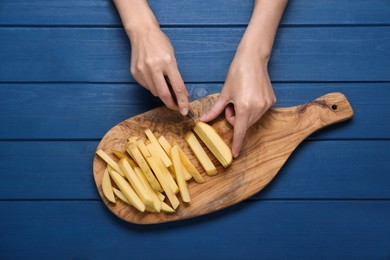 Photo of Woman cutting potato at blue wooden table, top view. Cooking delicious French fries