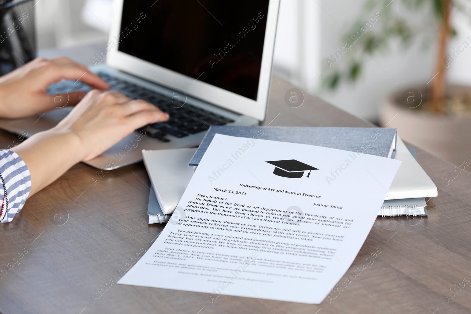 Photo of Student working with laptop at table indoors, focus on acceptance letter from university