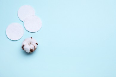 Photo of Cotton pads and flower on light blue background, flat lay. Space for text
