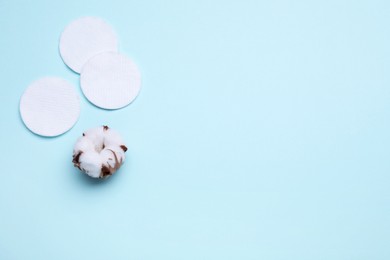 Cotton pads and flower on light blue background, flat lay. Space for text