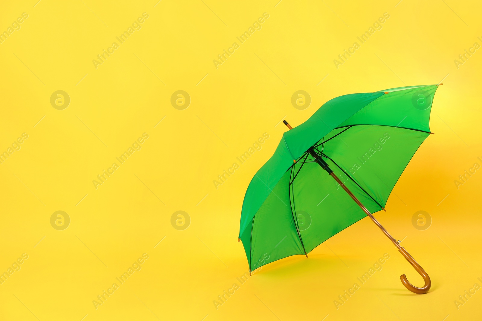 Photo of Beautiful green umbrella on light yellow background. Space for text