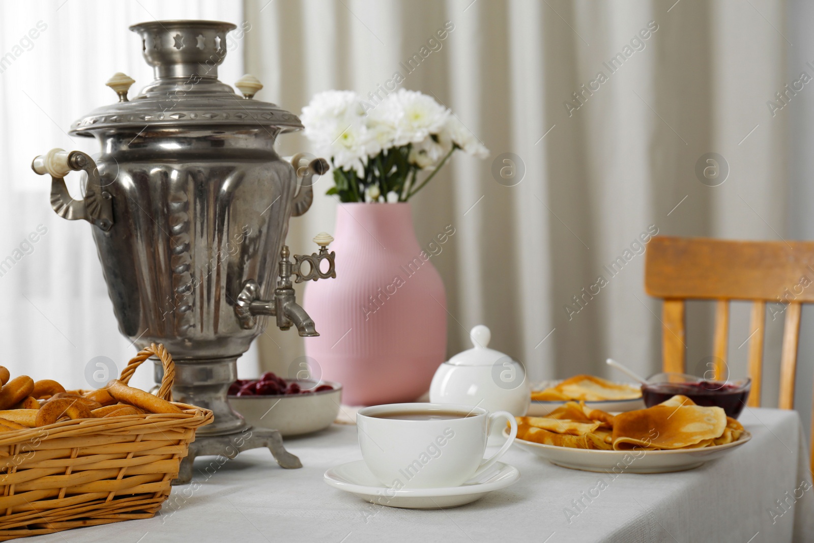 Photo of Vintage samovar, cup of hot drink and snacks served on table indoors. Traditional Russian tea ceremony