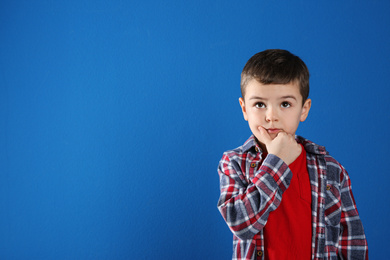 Photo of Thoughtful little boy on blue background, space for text
