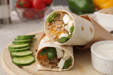 Delicious tortilla wraps with tuna, cucumber slices and sauce on wooden board, closeup
