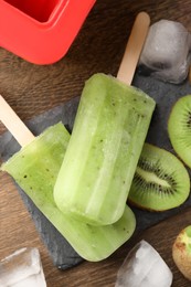Photo of Tasty kiwi ice pops on wooden table, flat lay. Fruit popsicle