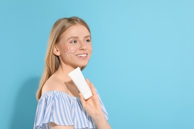 Photo of Beautiful young woman with sun protection cream on light blue background, space for text