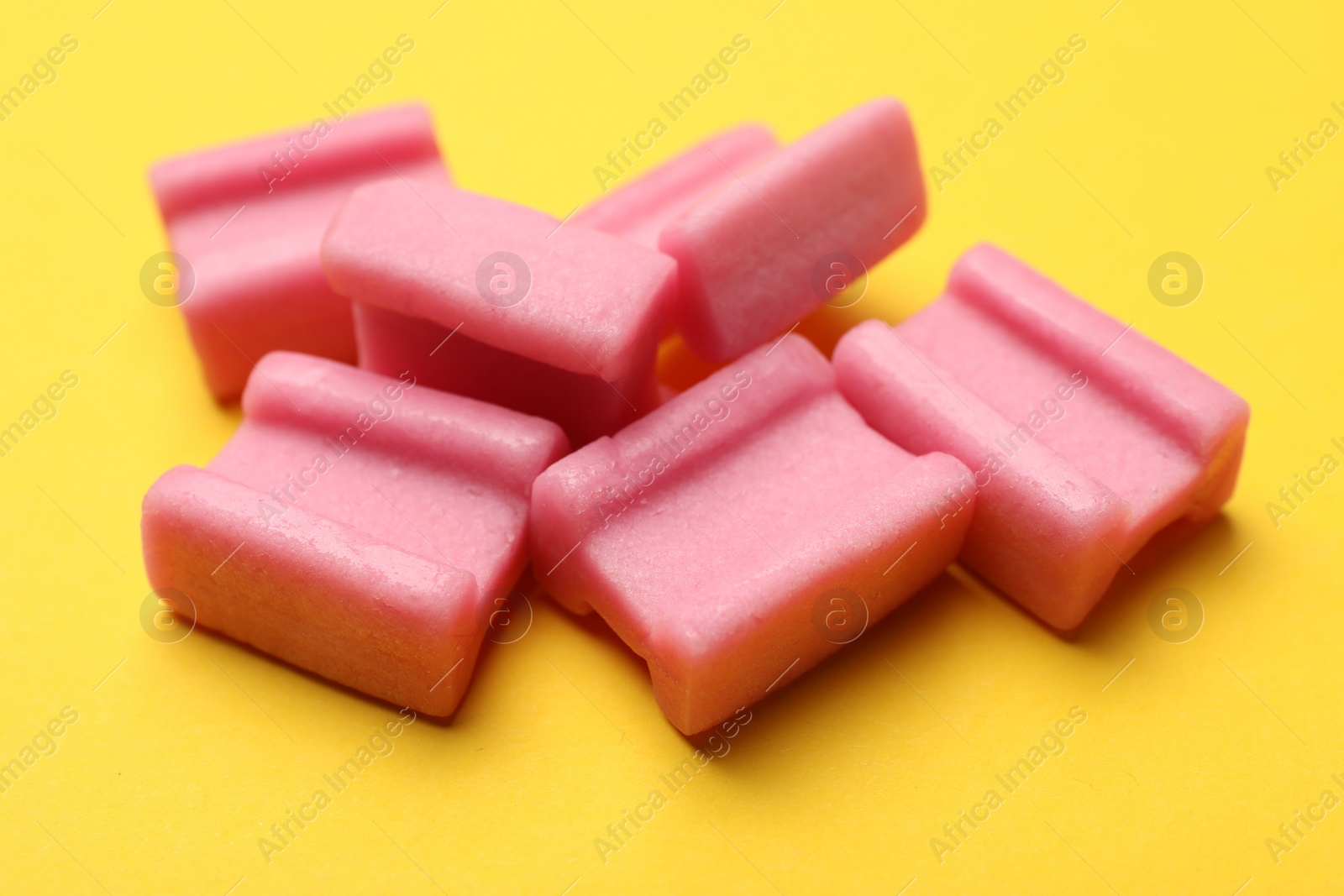 Photo of Tasty pink chewing gums on yellow background, closeup