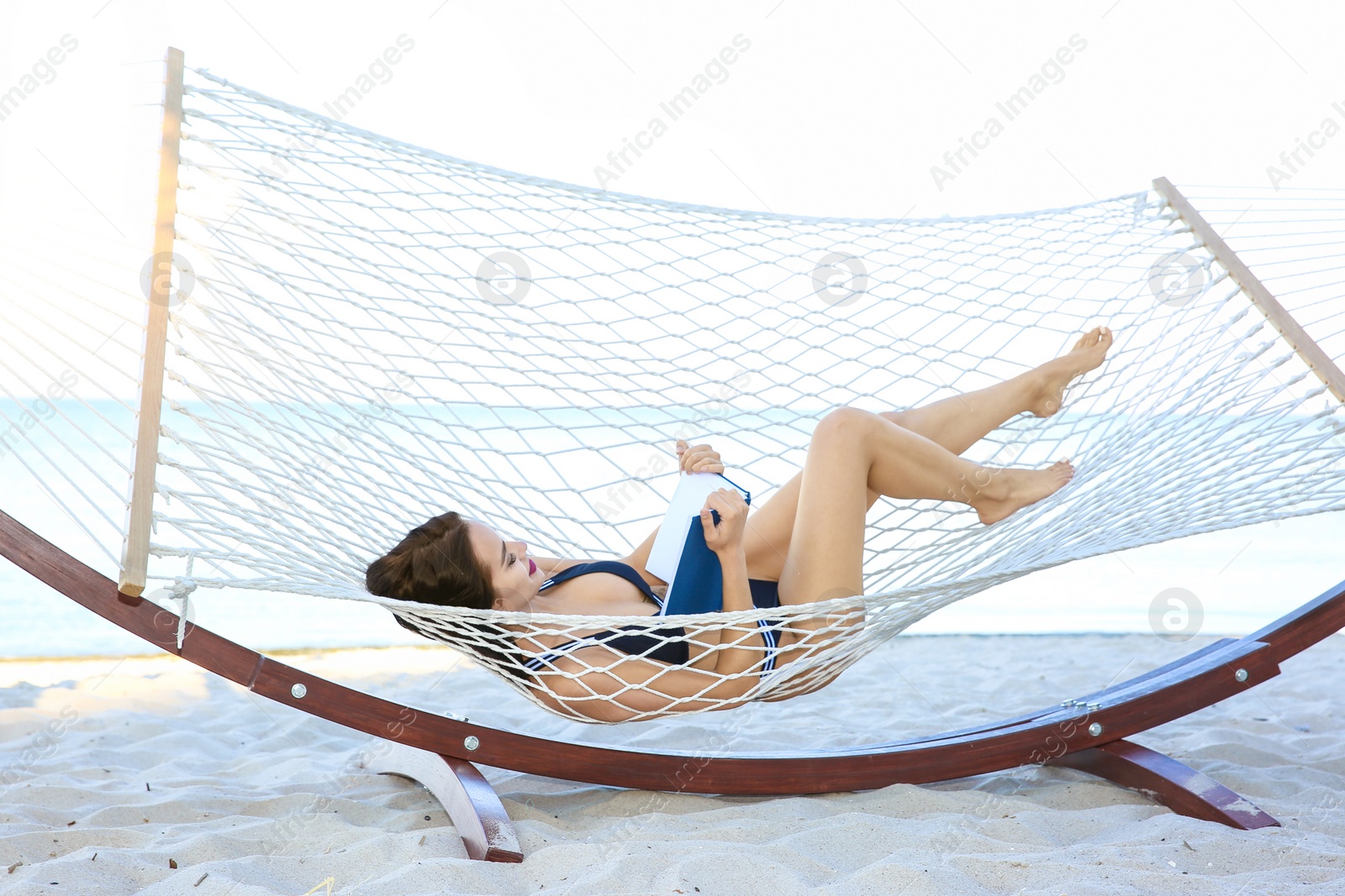 Photo of Young woman with book resting in hammock at seaside. Summer vacation