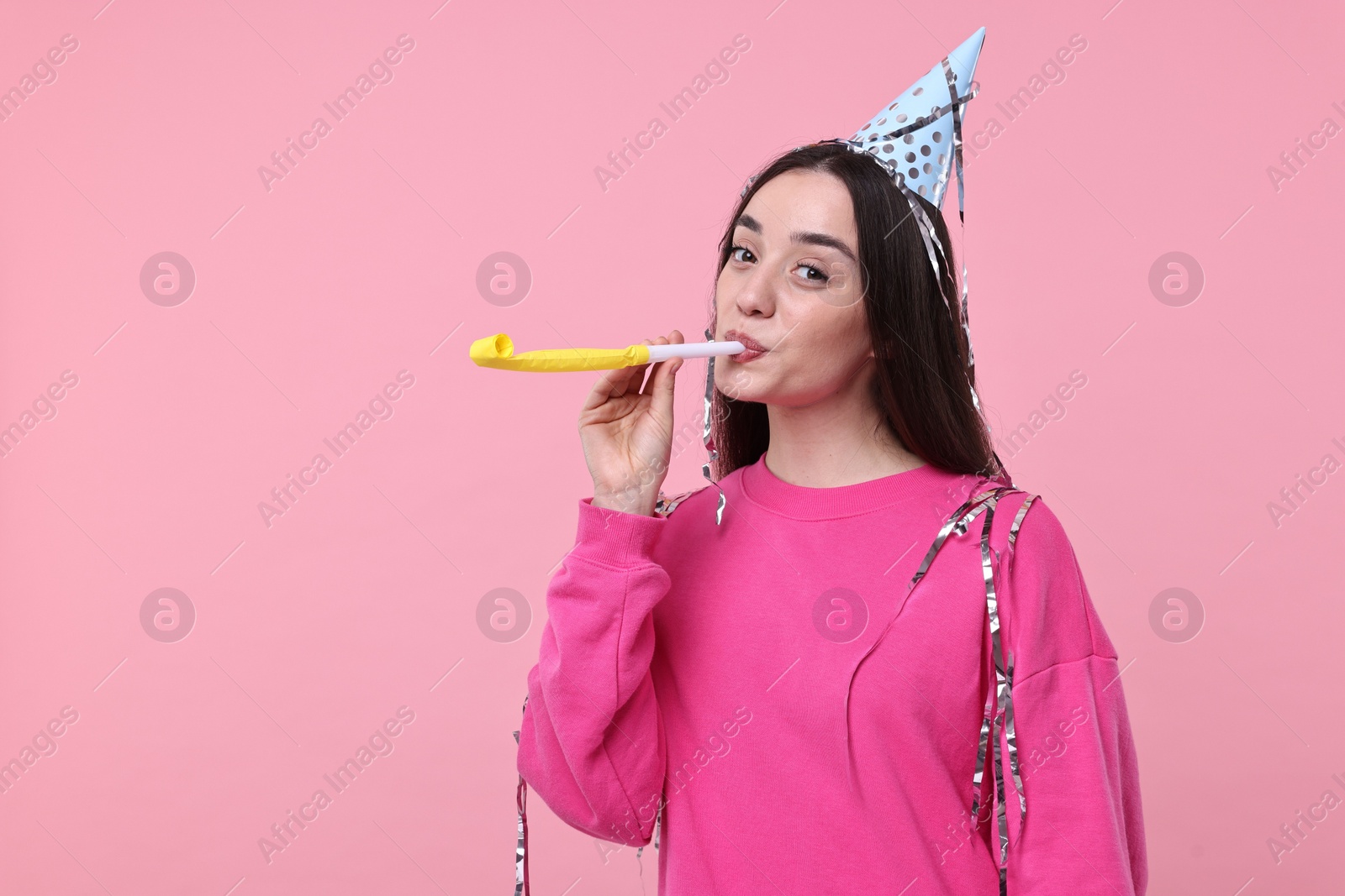 Photo of Woman in party hat with blower and streamers on pink background, space for text