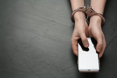 Photo of Man in handcuffs holding smartphone at black table, top view. Internet addiction