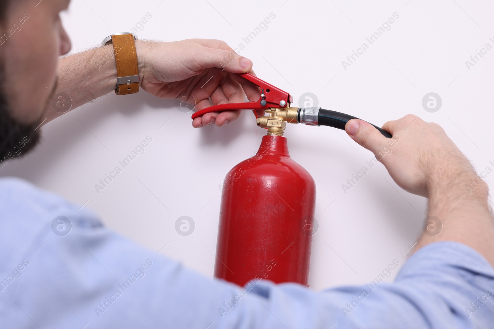 Photo of Man checking quality of fire extinguisher indoors, closeup