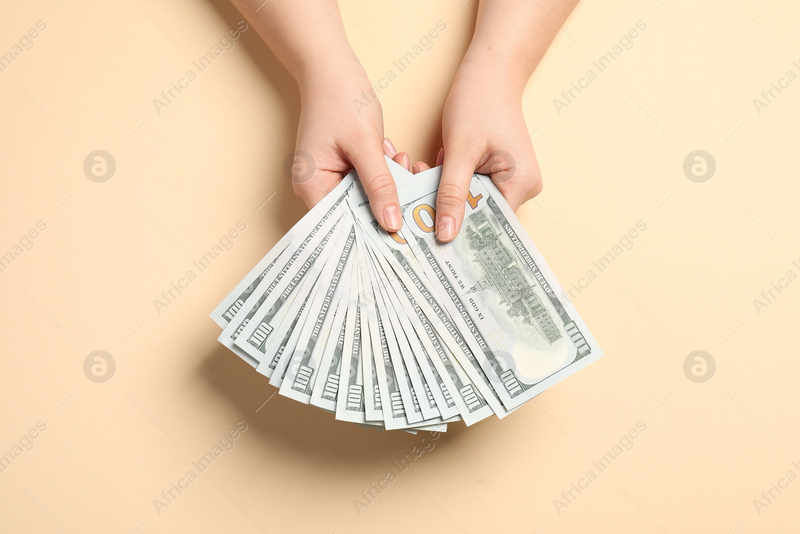 Photo of Money exchange. Woman holding dollar banknotes on beige background, top view