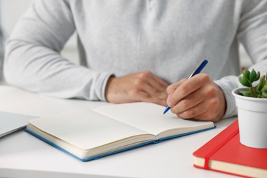 Photo of Young man writing in notebook at white table, closeup