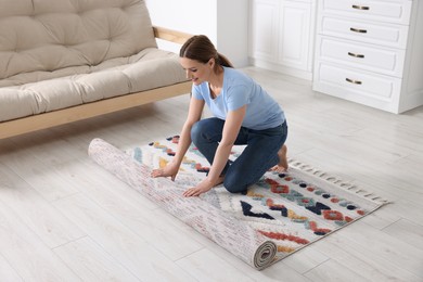 Smiling woman unrolling carpet with beautiful pattern on floor in room