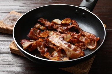 Delicious bacon slices in frying pan on wooden table, closeup