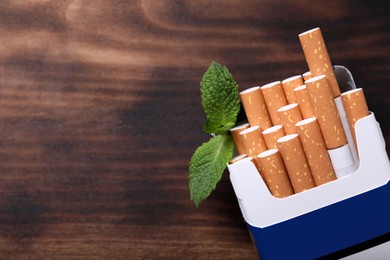 Photo of Pack of menthol cigarettes and mint leaves on wooden table, flat lay. Space for text
