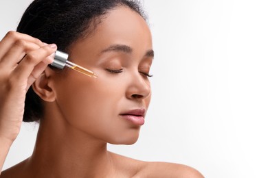 Photo of Beautiful woman applying serum onto her face on white background, closeup. Space for text