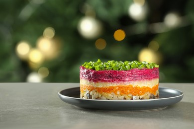 Photo of Herring under fur coat salad on grey table against blurred festive lights, space for text. Traditional Russian dish