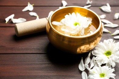 Photo of Golden singing bowl with flower and mallet on wooden table, closeup. Sound healing