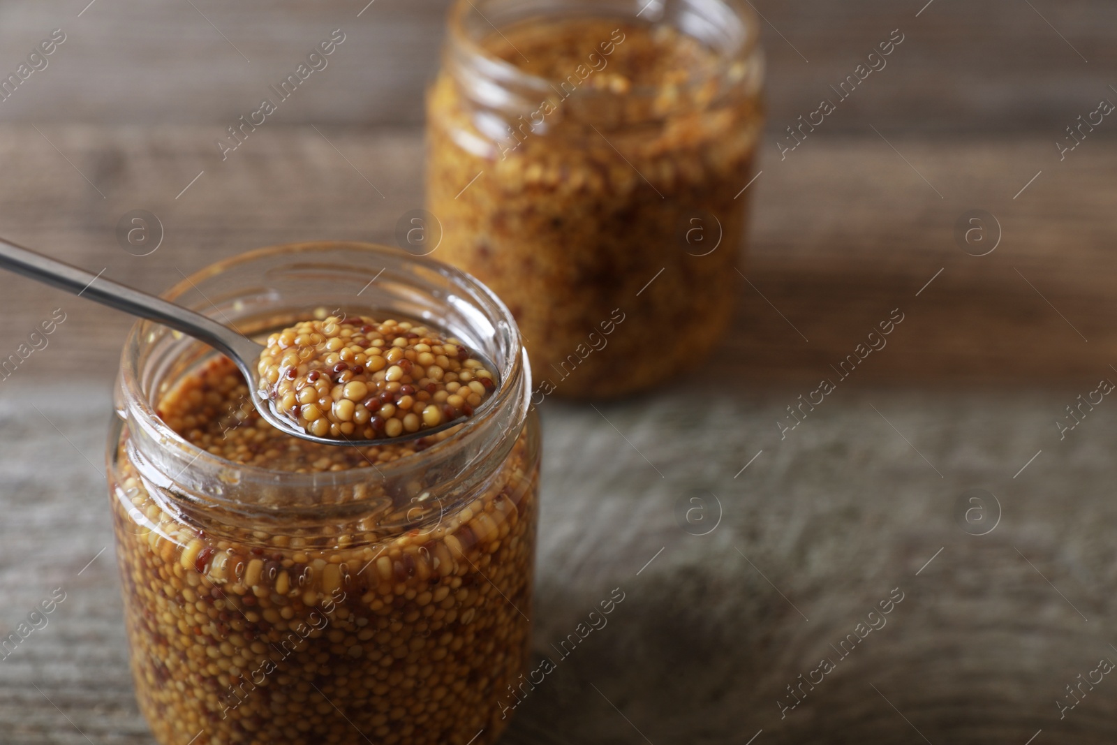 Photo of Jars and spoon of whole grain mustard on wooden table, closeup. Space for text