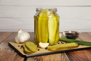 Jar with tasty pickled cucumbers and ingredients on wooden table