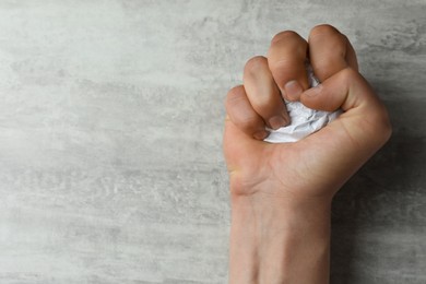 Photo of Angry man squeezing paper at table, top view. Space for text